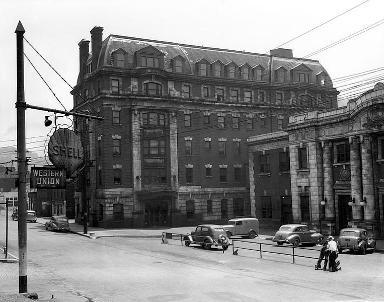 Black and white photograph of tall hotel and train station